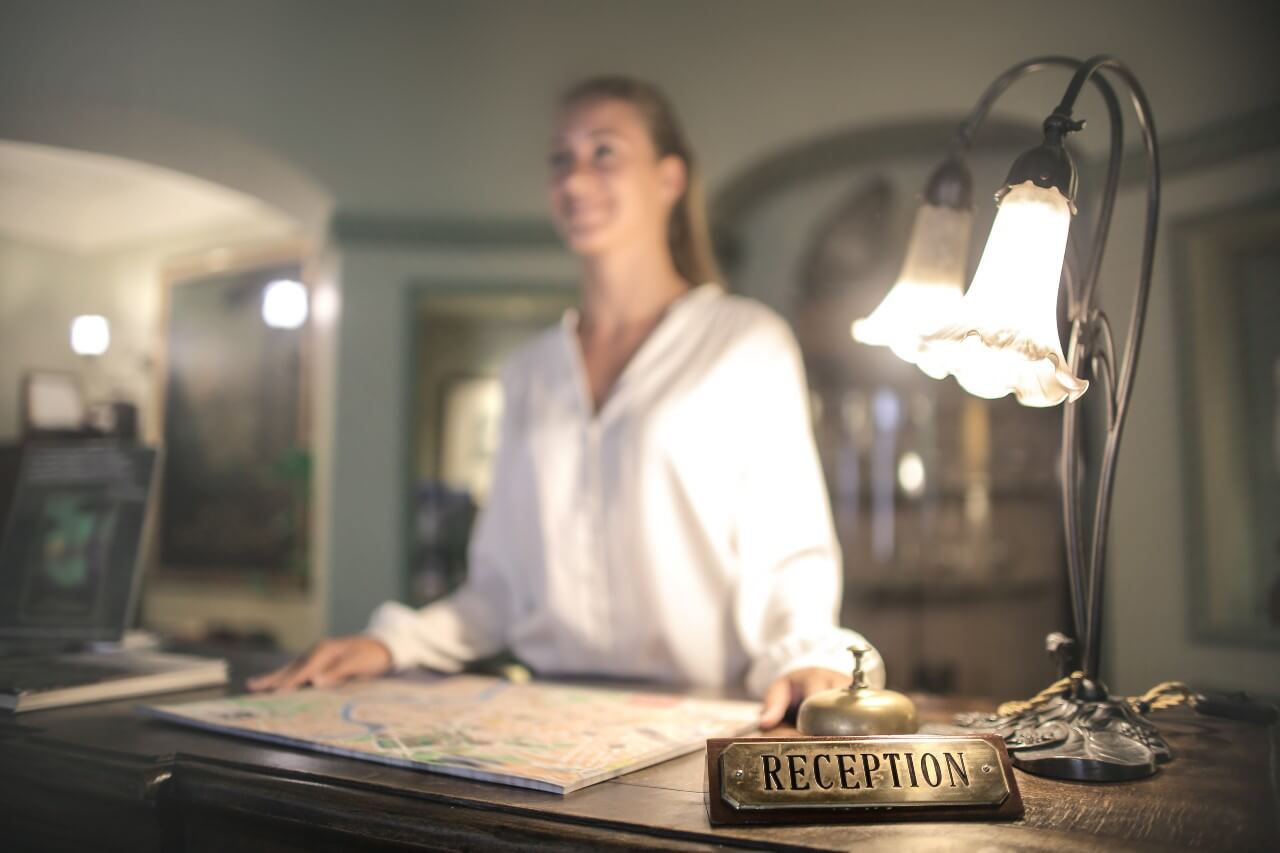 A lady wearing a white shirt stands behind a reception desk with a map in front of her