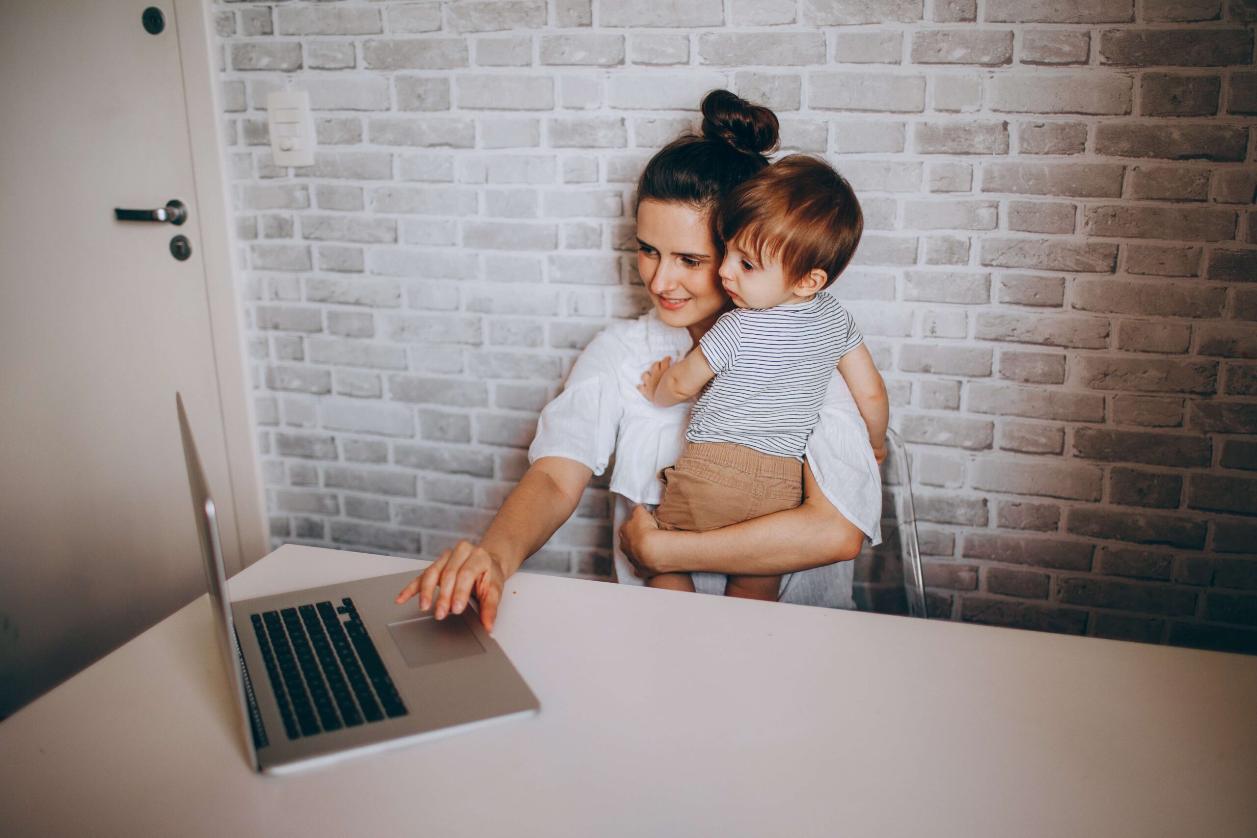 Working mother using a laptop whilst holding a child