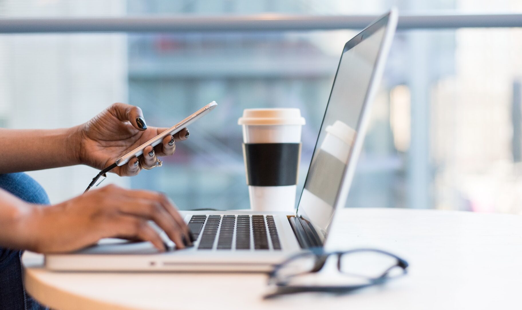 Woman holding phone while on laptop