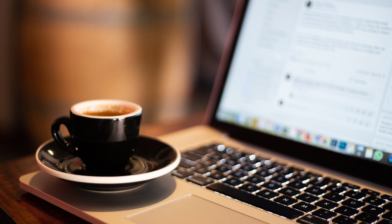 Laptop showing Facebook, and cup of coffee. Photo from Unsplash