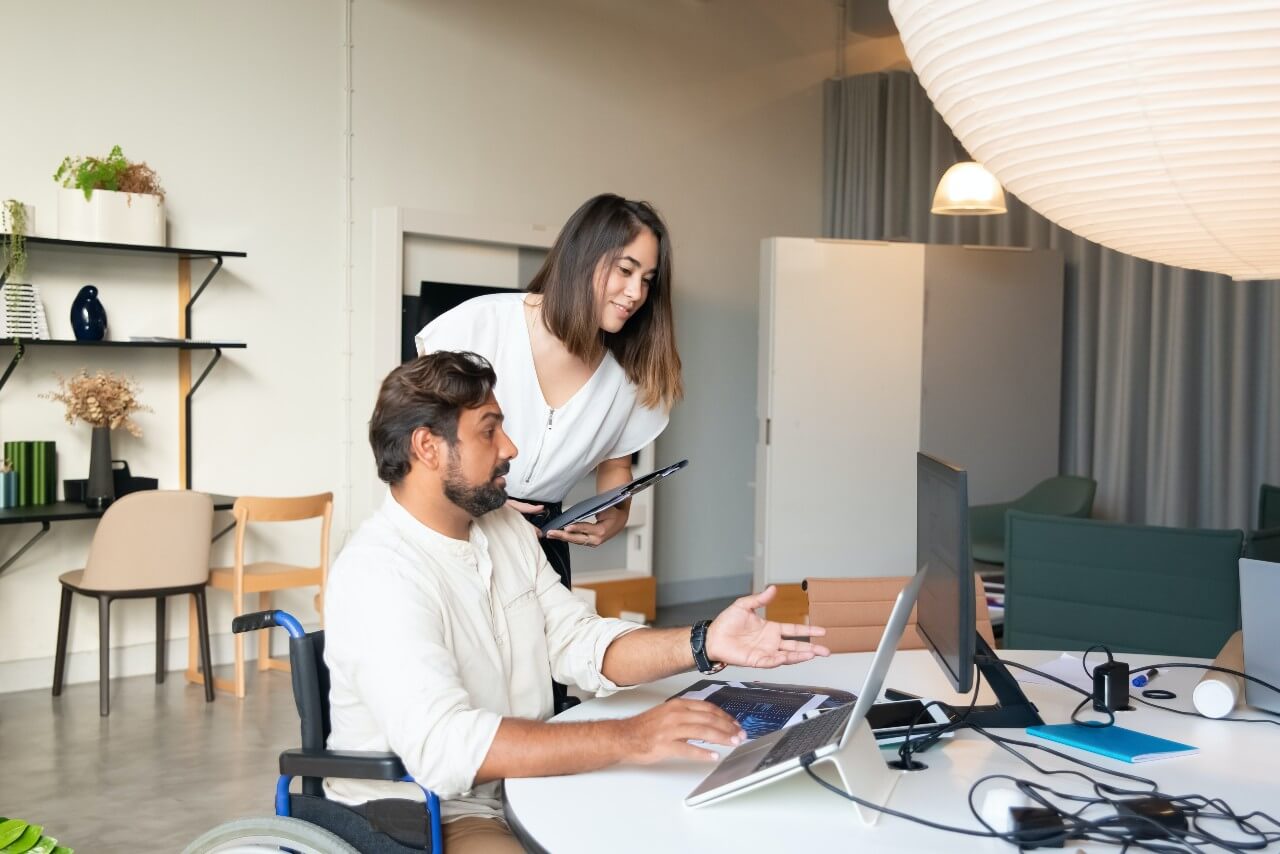 A man in a wheelchair works with his female colleague at a computer screen