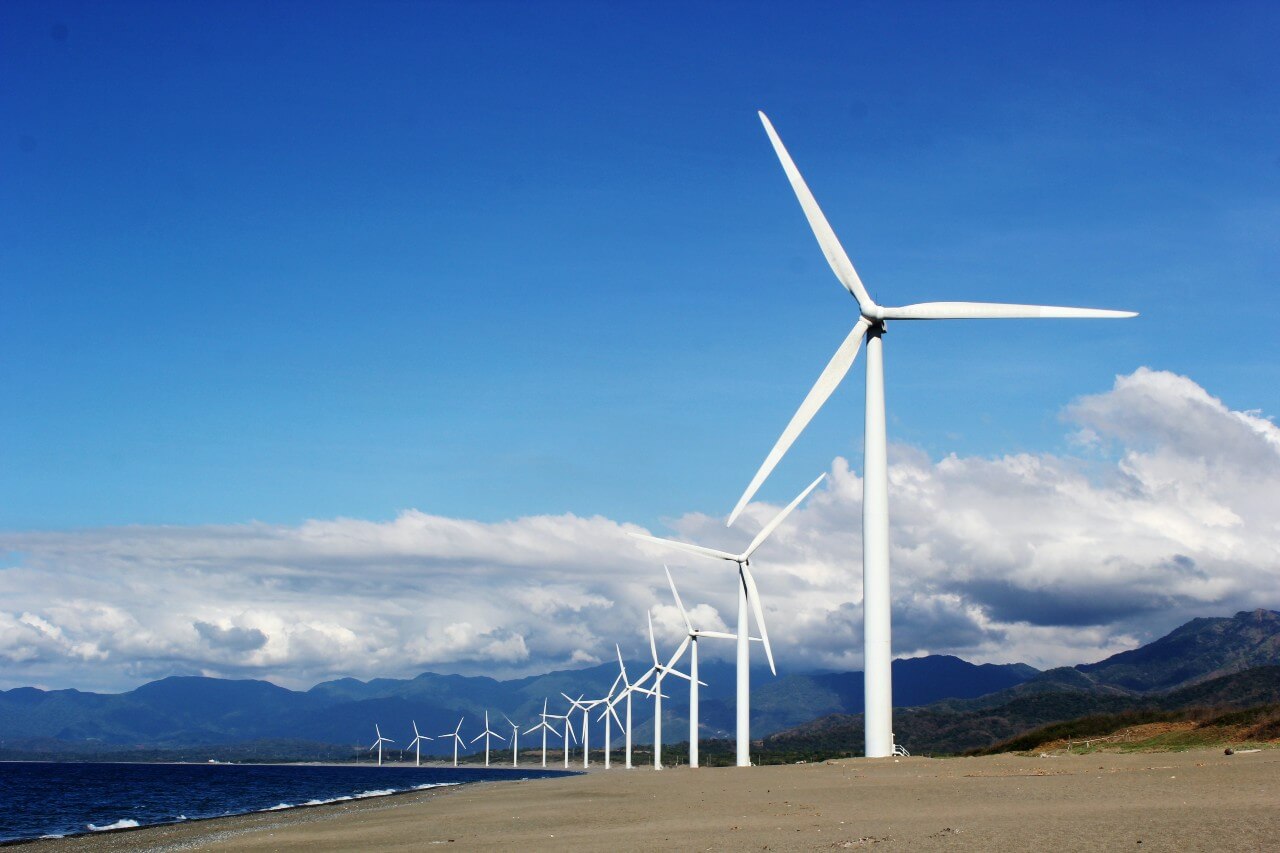 Image shows a line of wind turbines generating green energy, against a blue sky