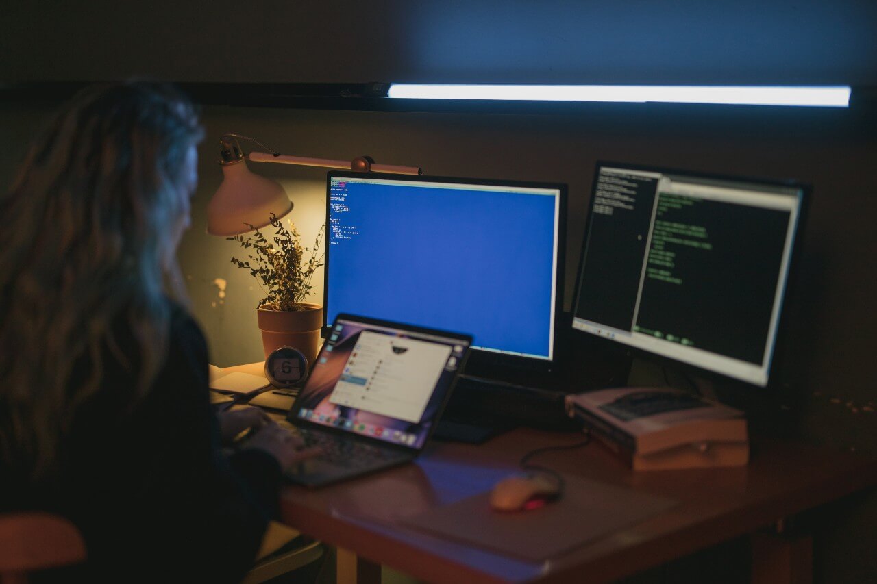 A woman works at her desk, using multiple computer screens