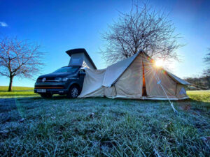 VW camper van parked in a field with a bell tent extension erected to the side