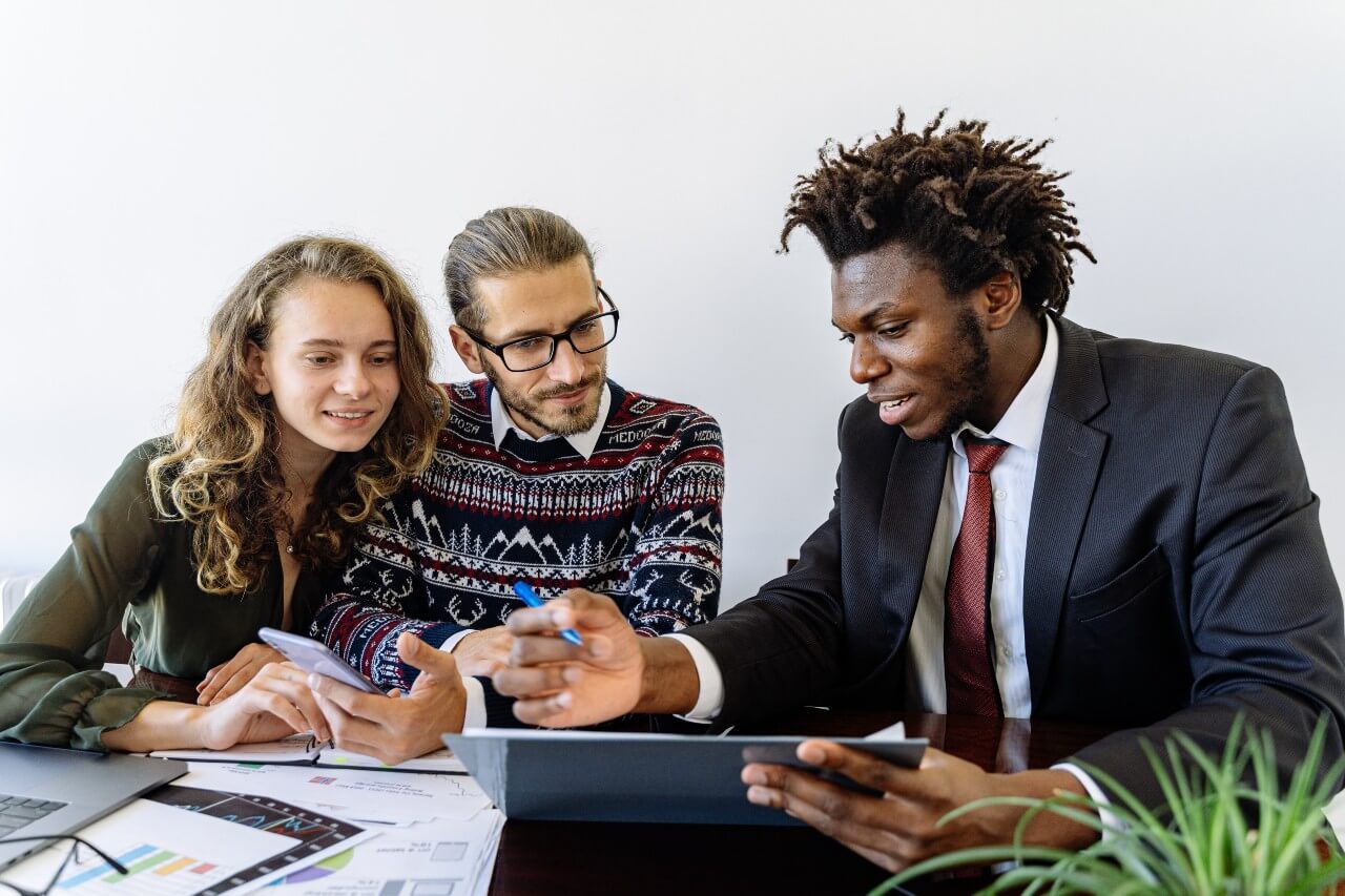 A black man wearing a suit and tie shows a white couple in casual clothes information on a clipboard