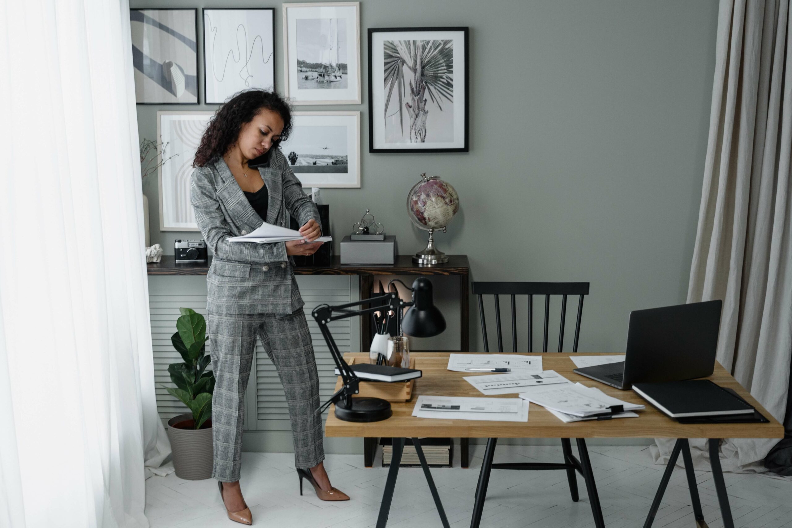 A lady in a grey suit stands looking at paperwork while on the phone