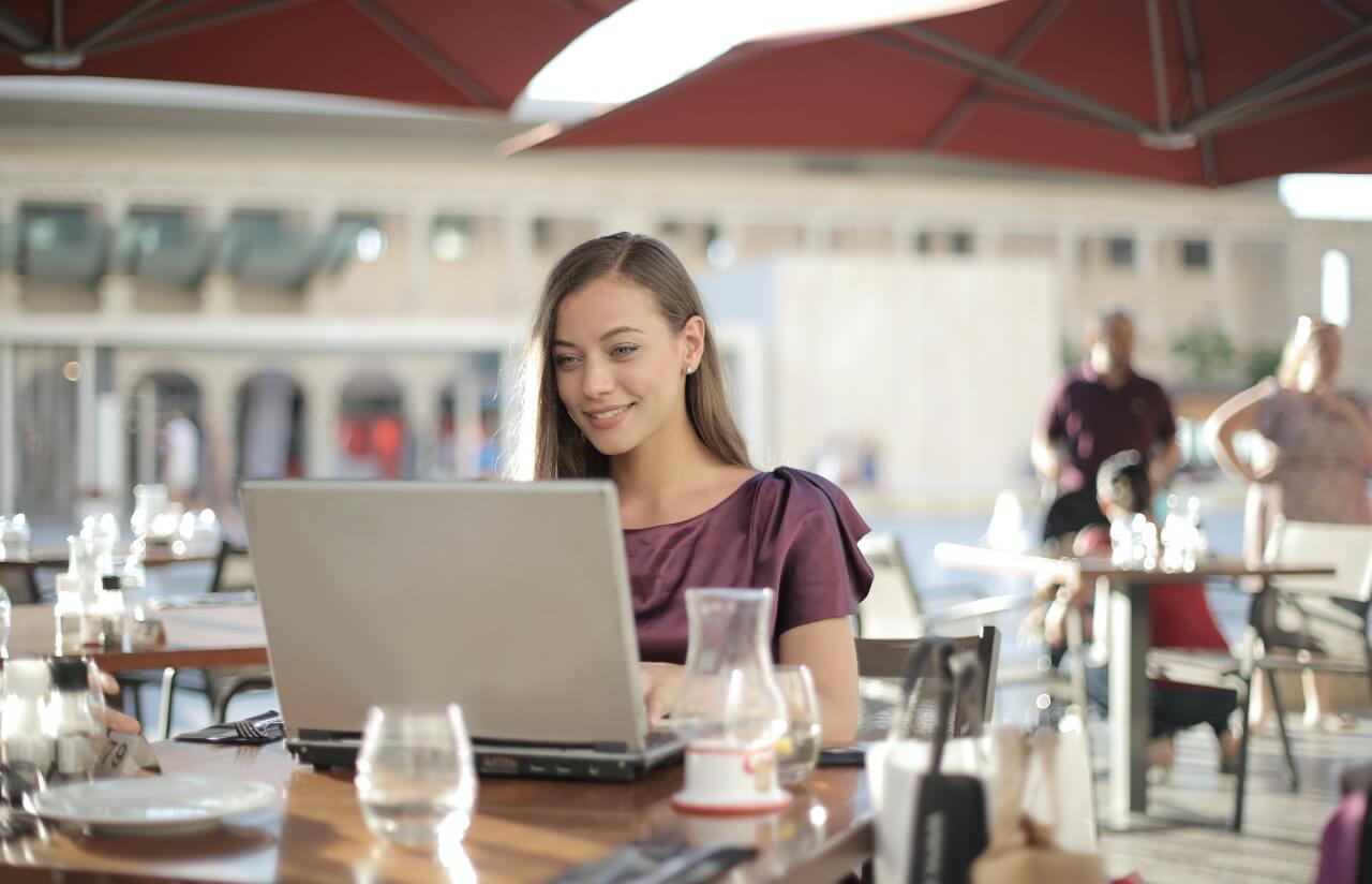 Lady wearing purple top sits in cafe working at a laptop